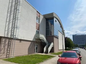 Budova se sportovní halou v ulici Heyrovského se schodištěm ke vchodu. Před budovou jsou zaparkovaná auta.