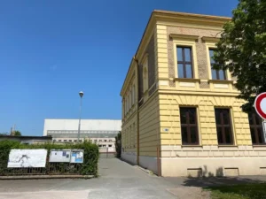 Vjezd ke sportovní hale v Kuklenách se žlutou budovou školy v pravé části.